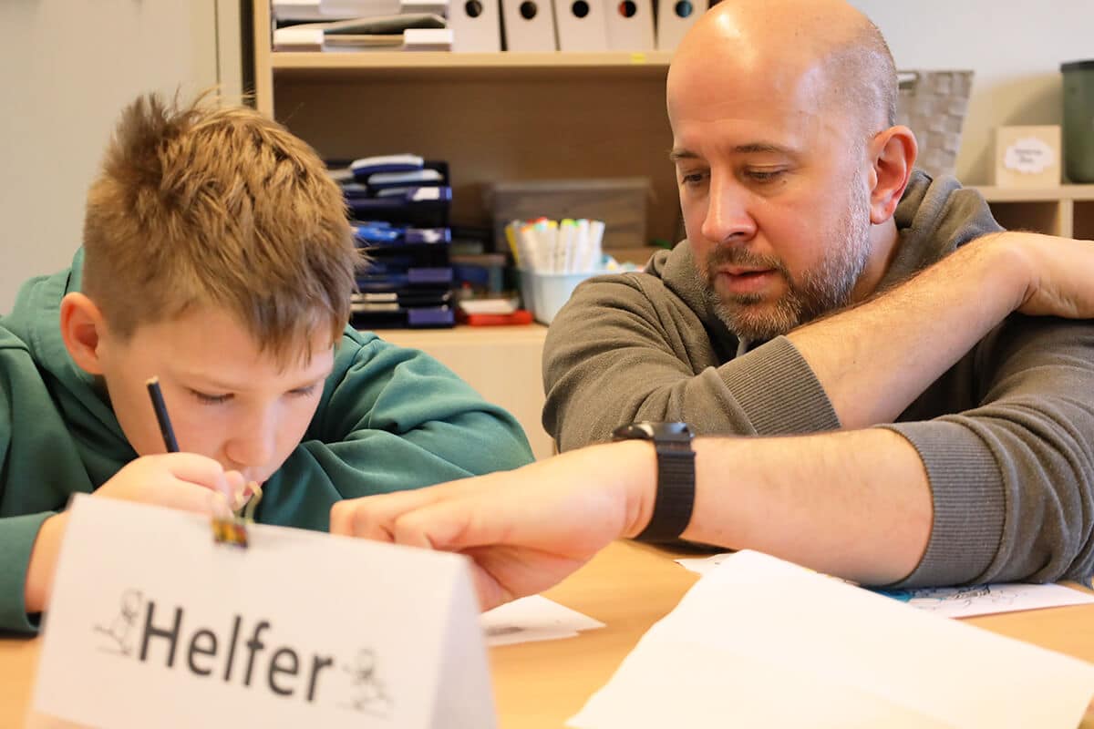 Lehrer sitzt mit Schüler konzentriert am Tisch und unterstützt bei der Arbeit