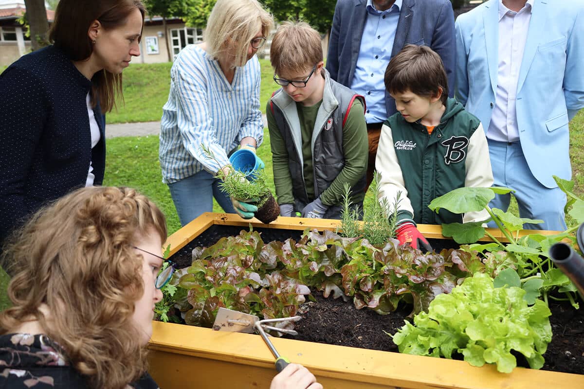 Gruppe von Kindern und Erwachsenen beim Pflanzen in einem Hochbeet im Freien